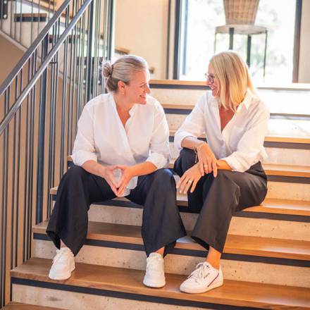 Zwei Frauen sitzen auf einer Treppe und unterhalten sich 